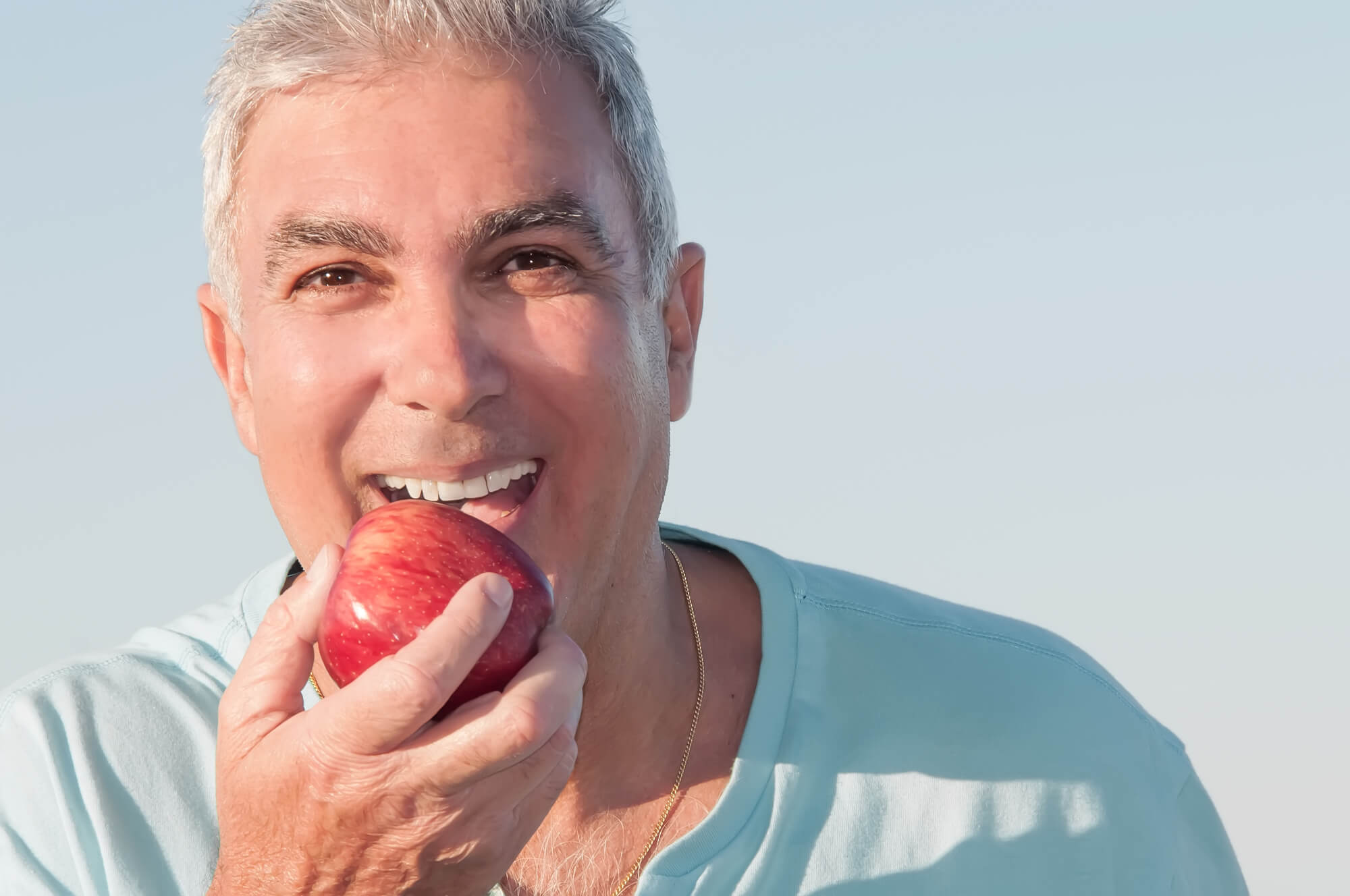 Man wearing Fort Pierce Dentures bitting an apple